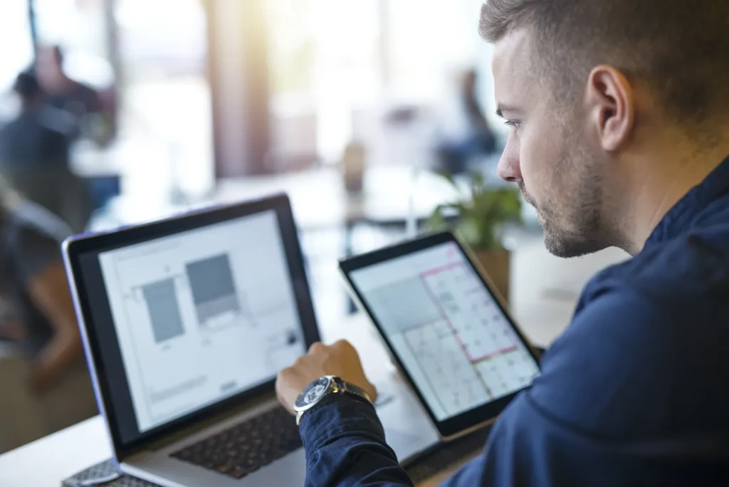 Uomo in ufficio che confronta i dati di un software sul portatile e sul tablet